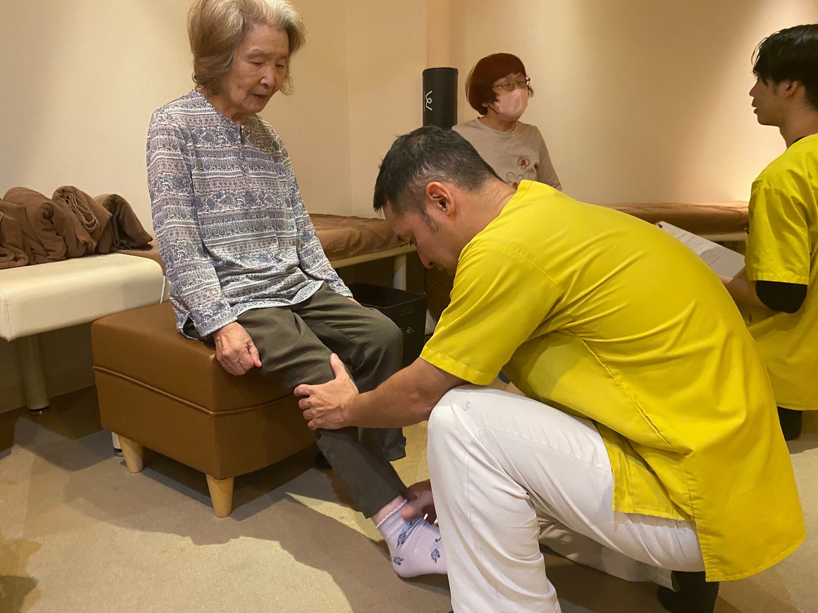 体操教室で、スタッフが椅子に座った参加者の膝の伸び方を確かめている様子