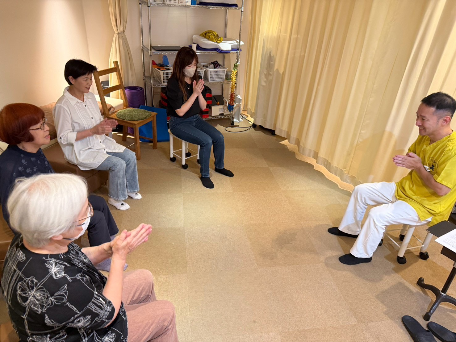 体操教室で、輪になって座った参加者とスタッフが手をたたいている様子