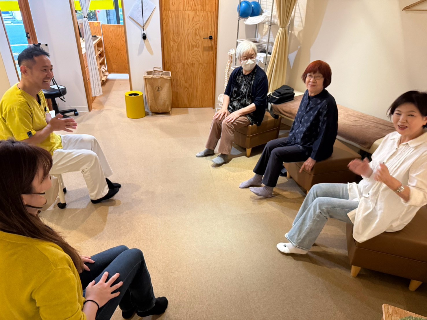 体操教室の合間に、進行役の鈴木と参加者が笑顔で話している様子