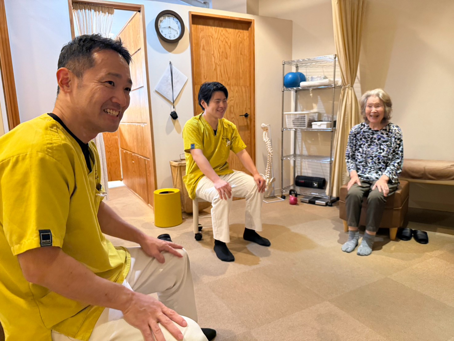 体操教室で、椅子に座ったスタッフと参加者が笑い合っている様子