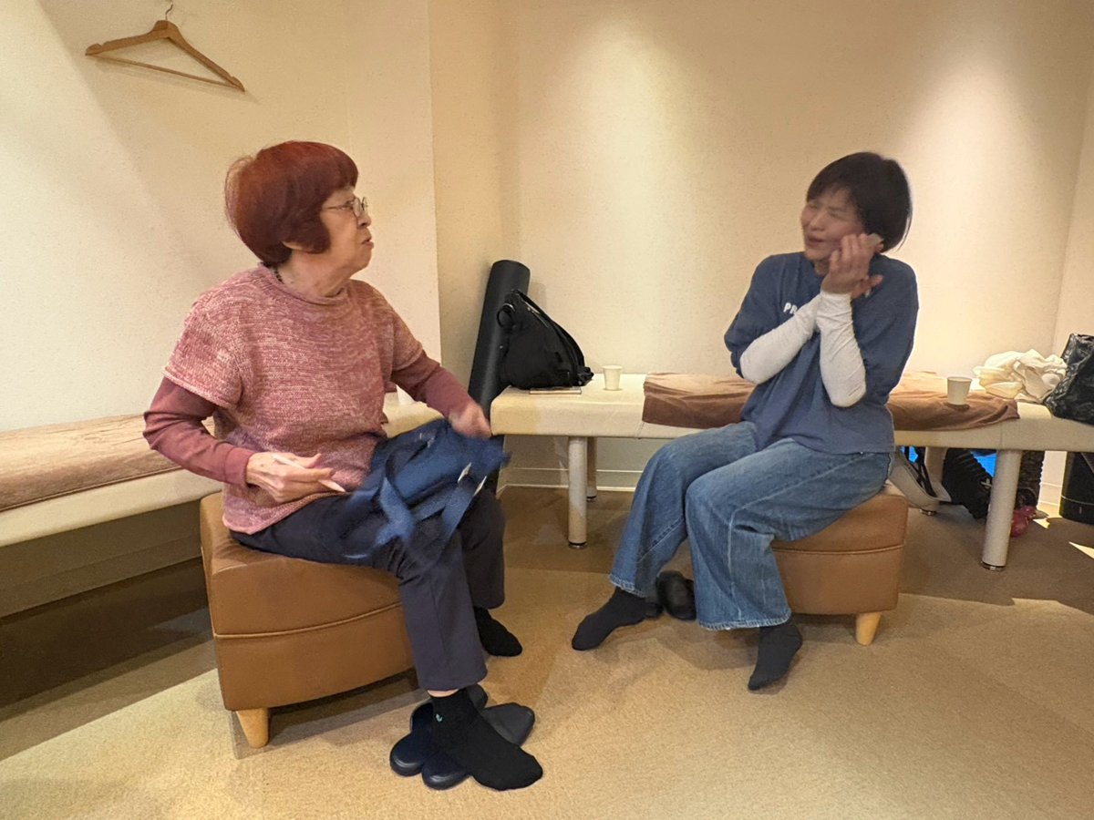 体操教室の合間に、椅子に座った参加者2名が向かい合って談笑している様子